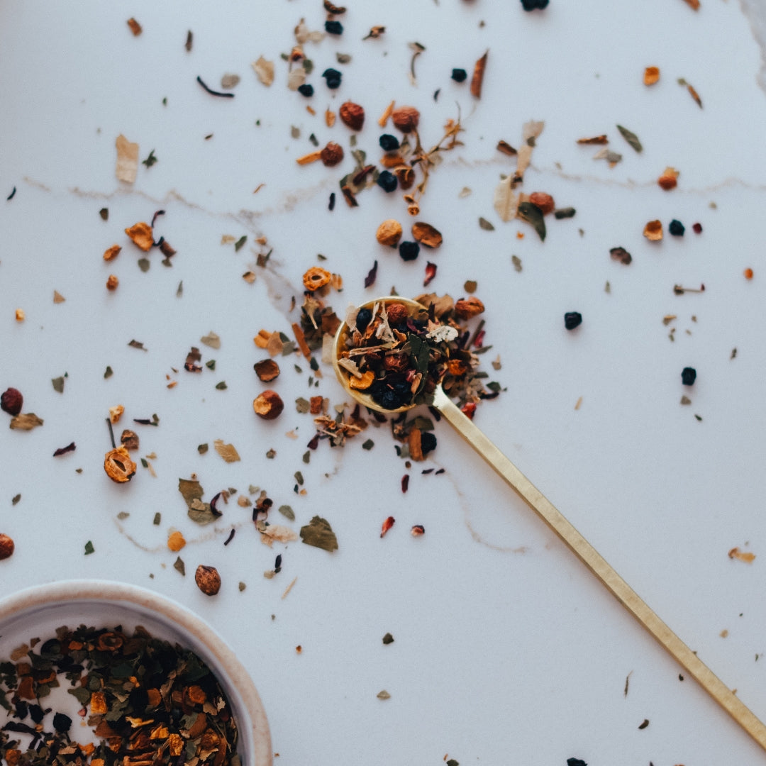 Medicinal herb blend on a white surface with a wooden spoon