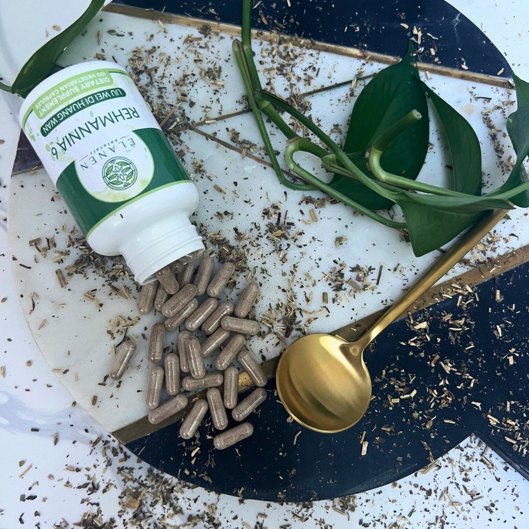Supplement bottle with capsules on a decorative plate with herbs and a gold spoon.