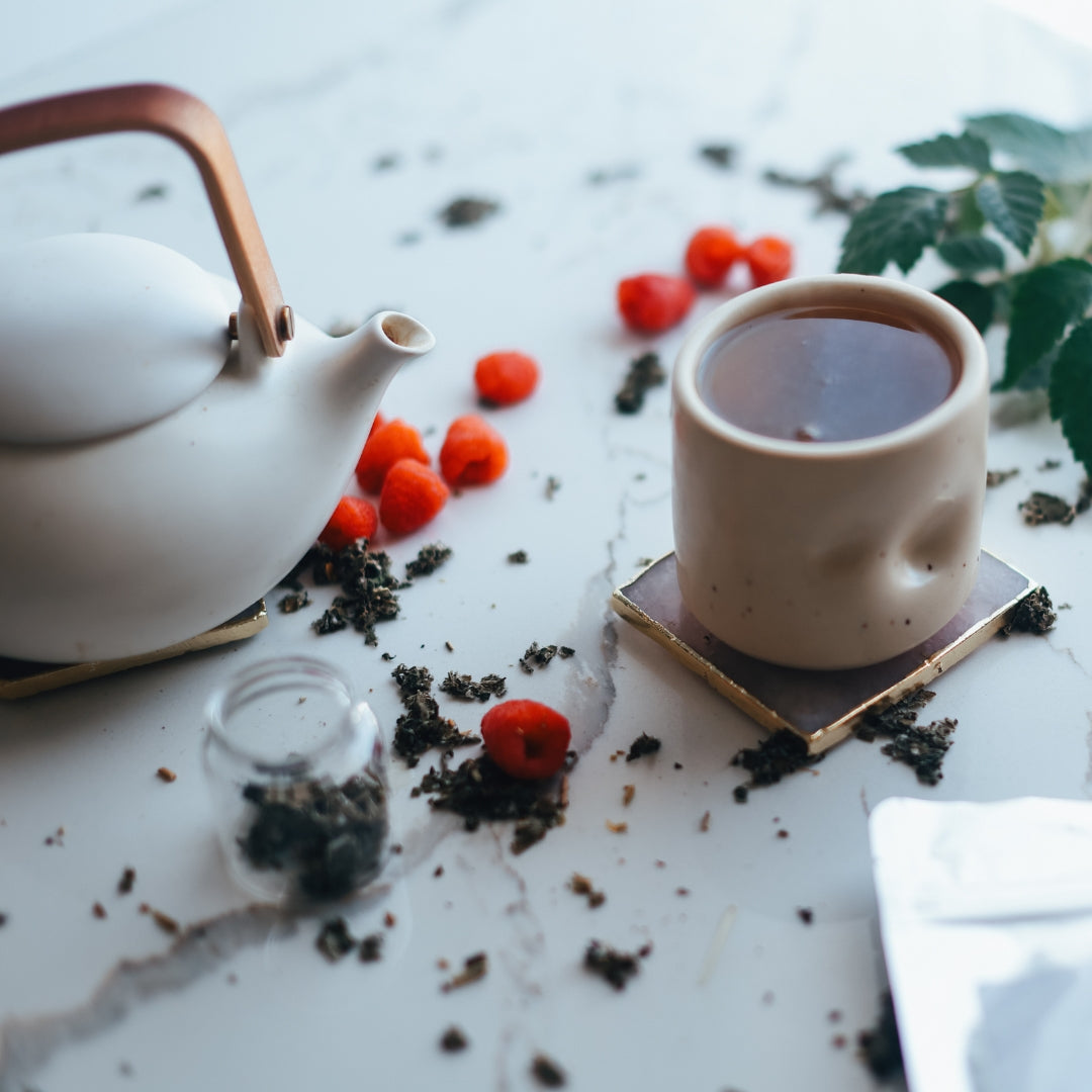 Tea set with a teapot, cup, and tea leaves on a light surface.