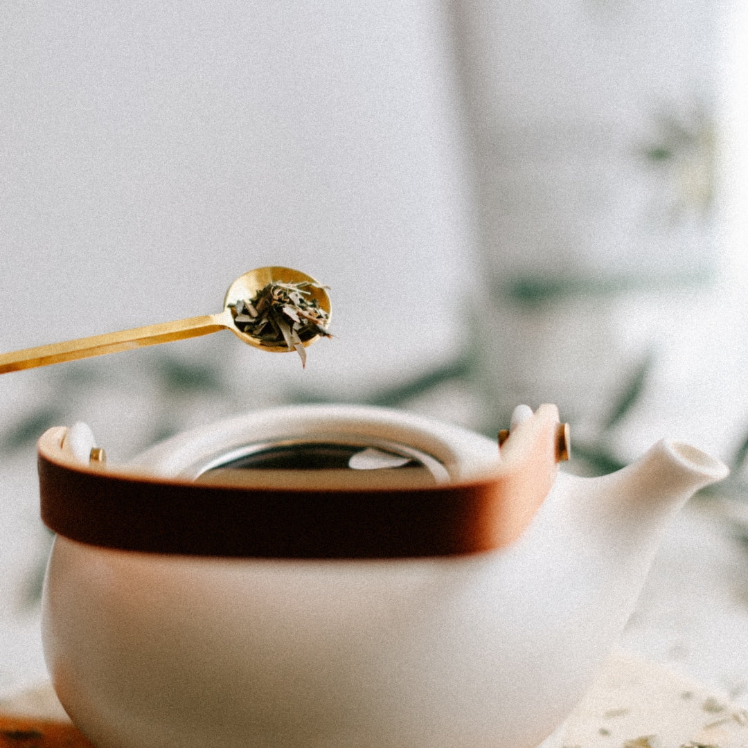 Tea leaves being added to a teapot with a blurred background