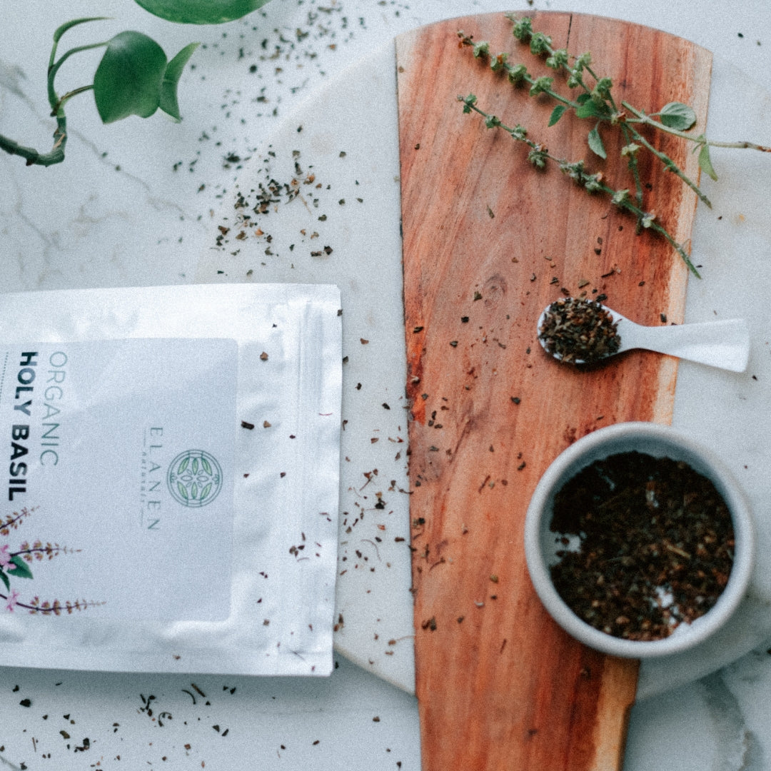 Organic holy basil package on a marble surface with a wooden cutting board and herbs.
