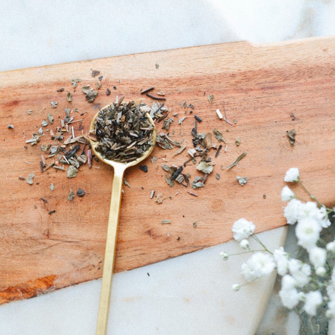 Gold spoon with dried plantain leaf on a wooden board with white flowers in the background