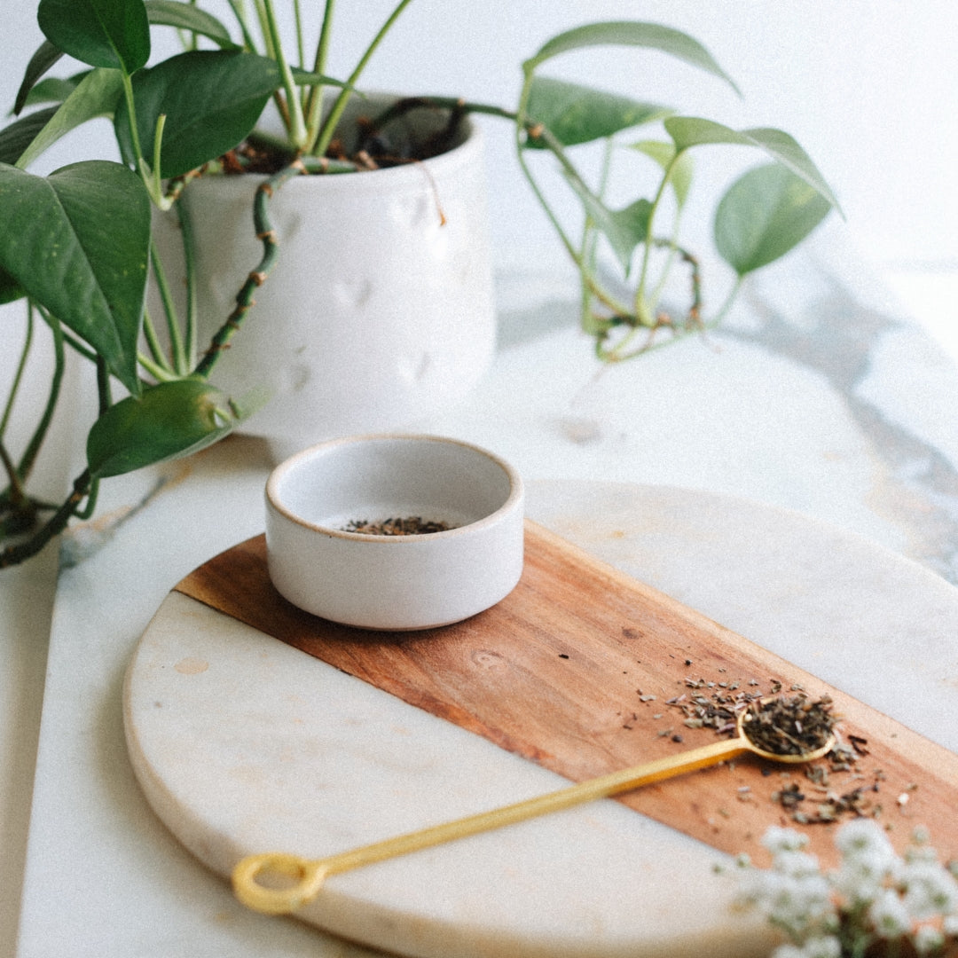 Ceramic bowl with plantain leaves on a wooden board with a marble surface, potted plant in the background.
