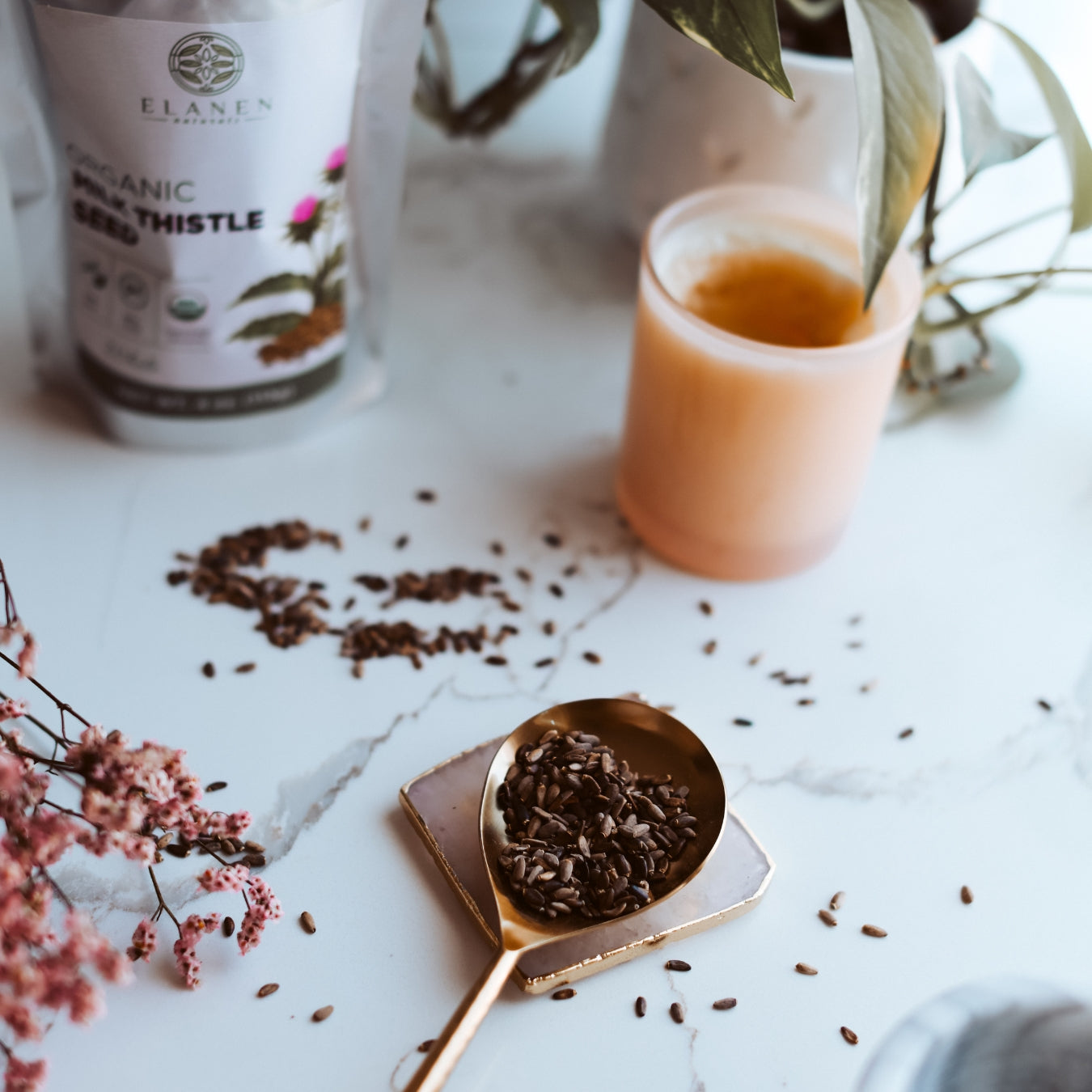 Candle, spoon with milk thistle seeds, and package on a marble surface