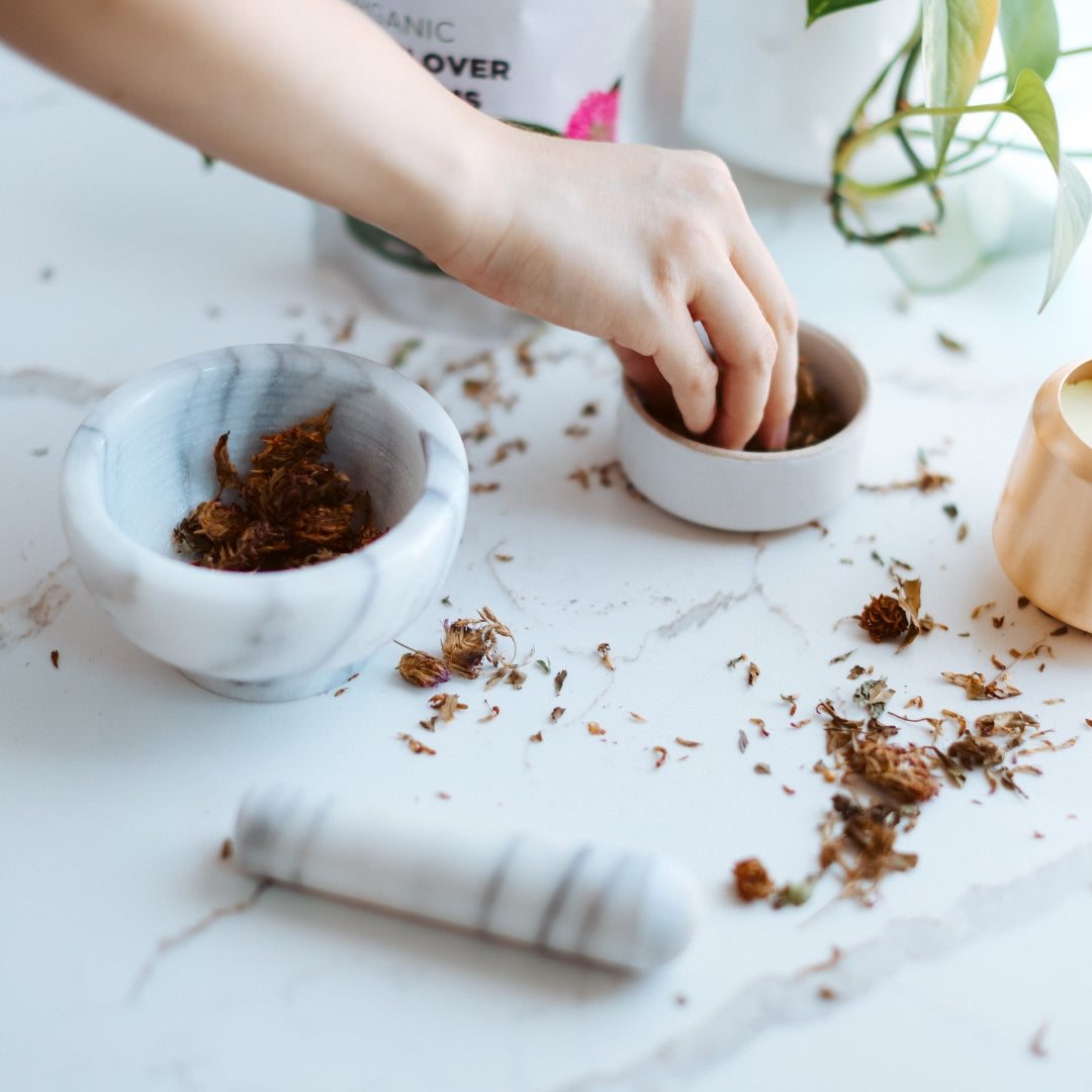Person handling dried red clover in small bowls on a marble surface