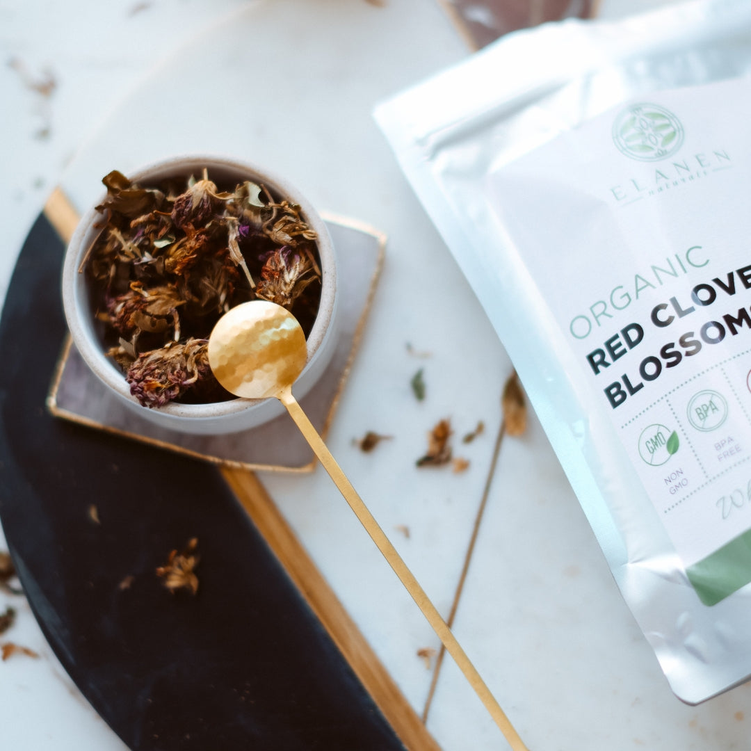 Red clover blossoms in a cup with a spoon and organic tea packaging on a marble surface
