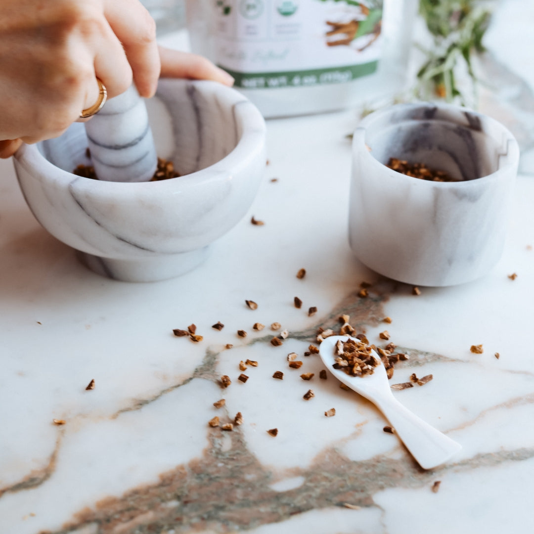Person using a mortar and pestle on a marble surface with dandelion root.