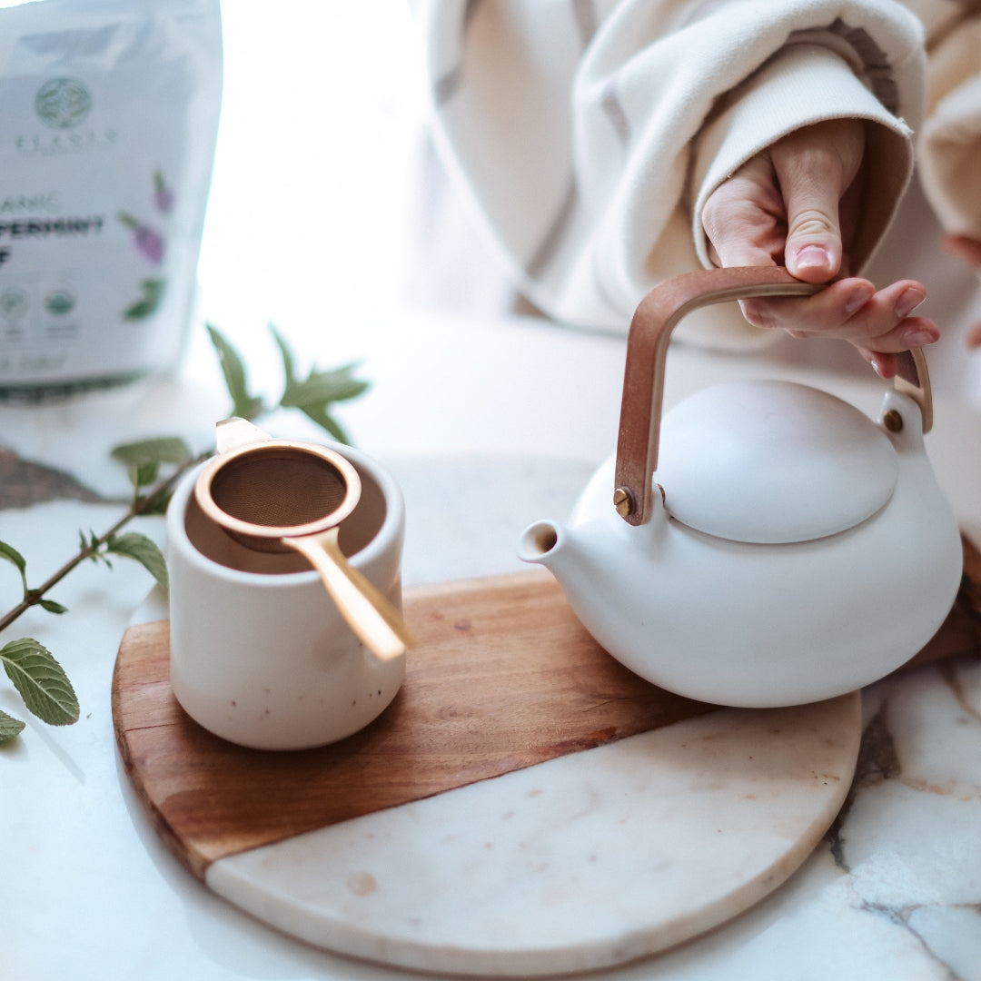 White teapot and cup on a wooden coaster with a marble surface
