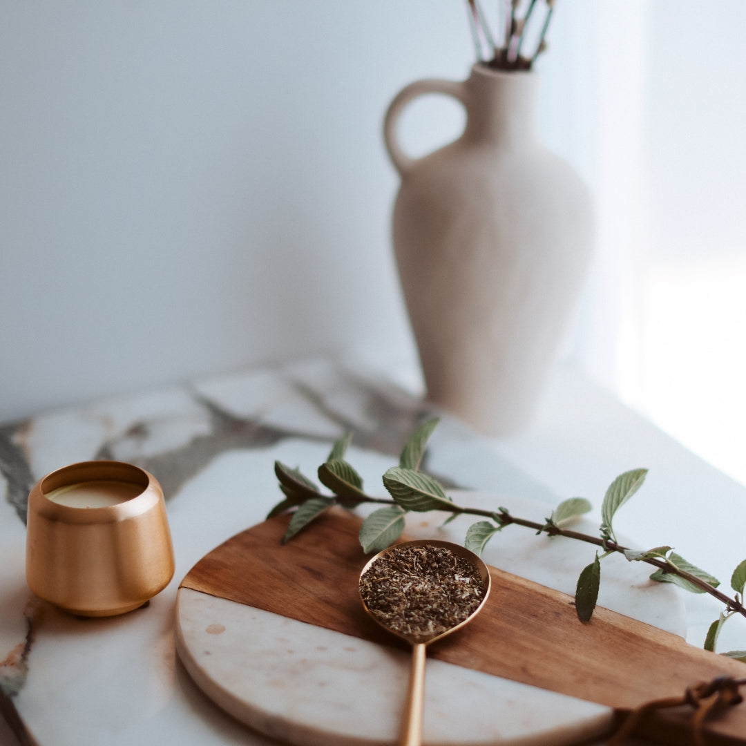 Wooden spoon with dried peppermint leaf on a marble surface with a vase in the background