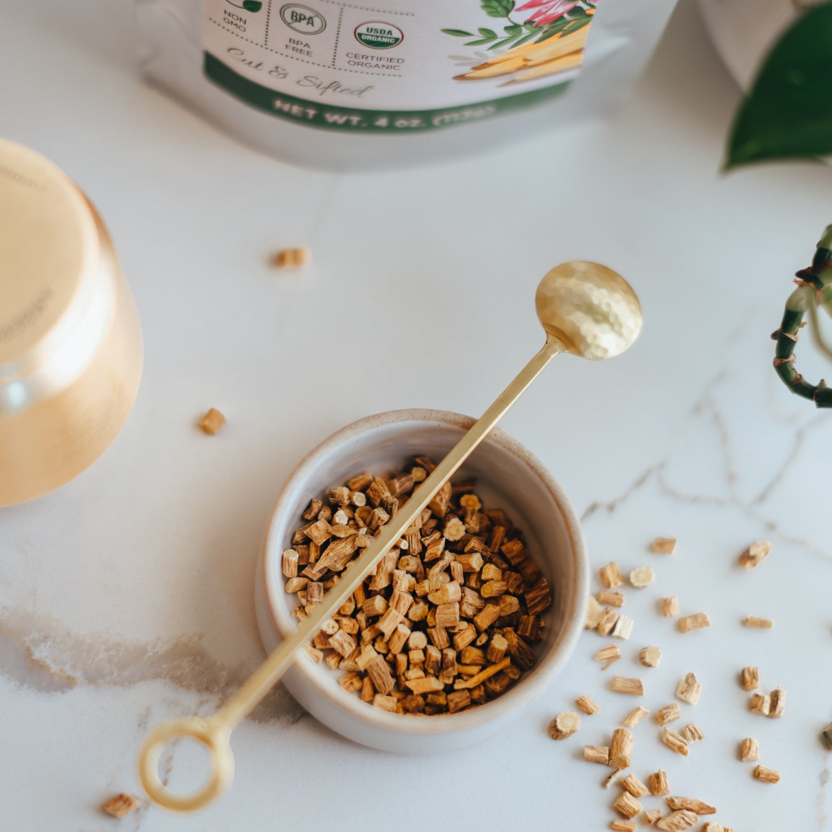 Small bowl with dried astragalus root and a gold spoon on a marble surface.