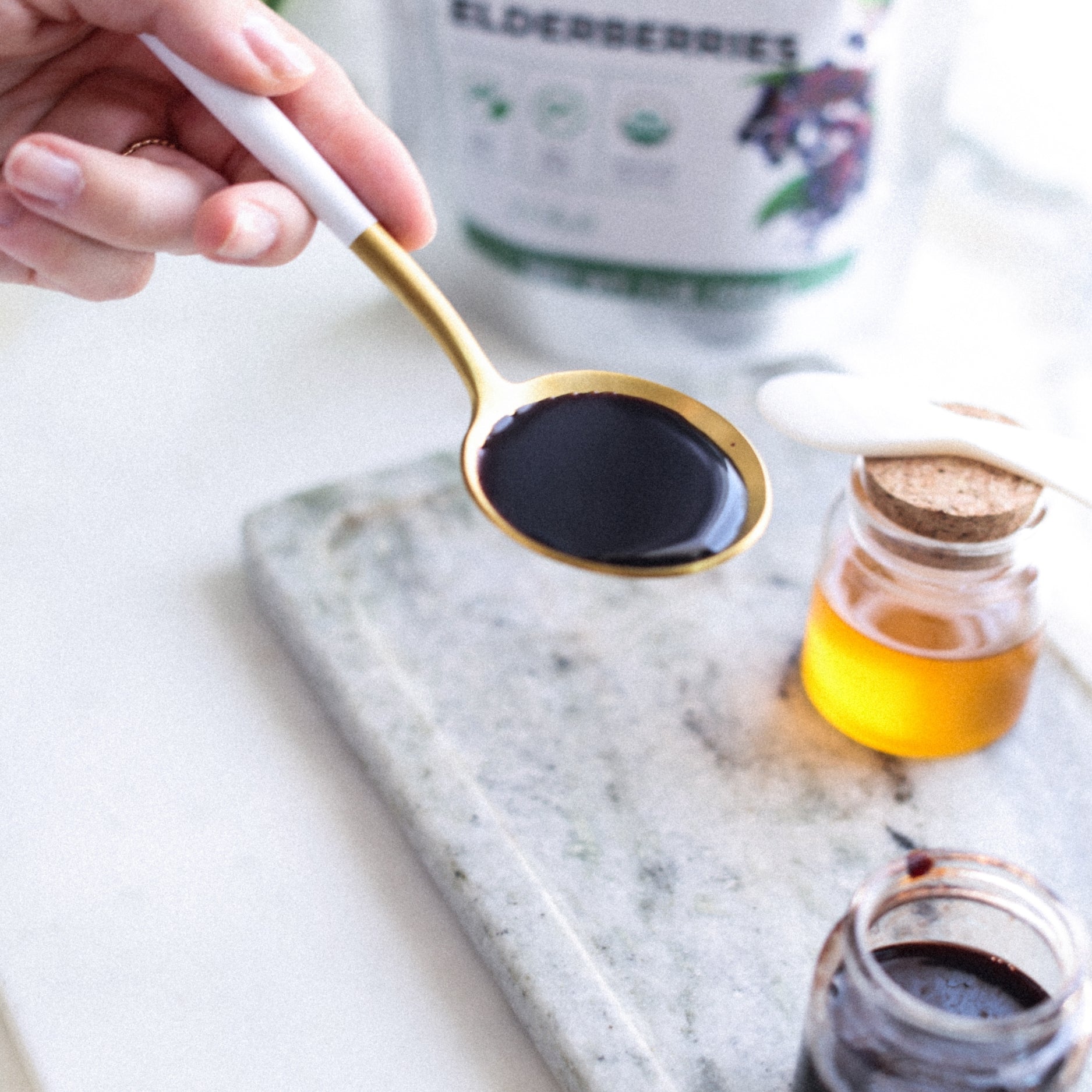 Spoon with elderberry syrup on a marble surface with jars and bottles in the background