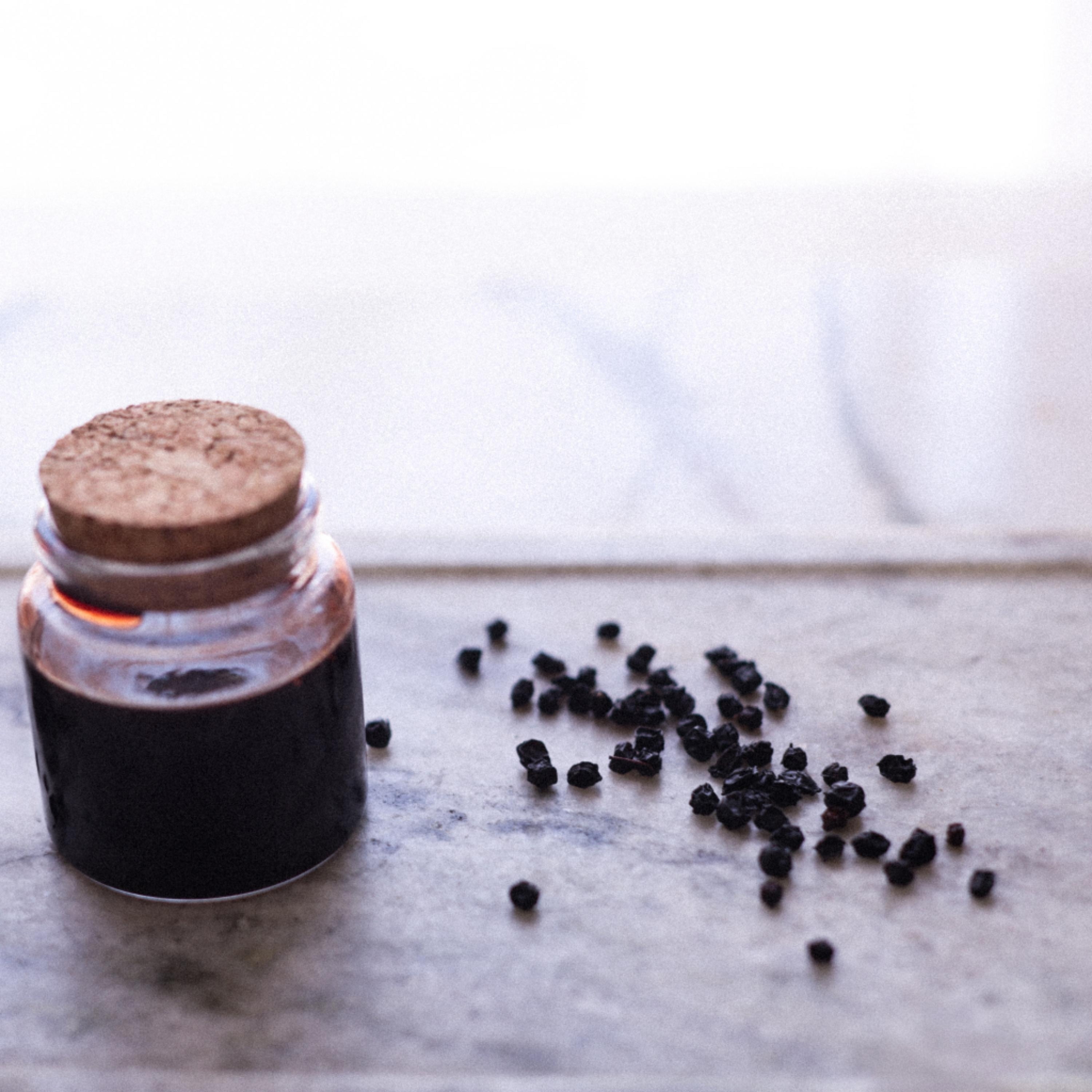 Jar of elderberry syrup with a cork lid on a marble surface