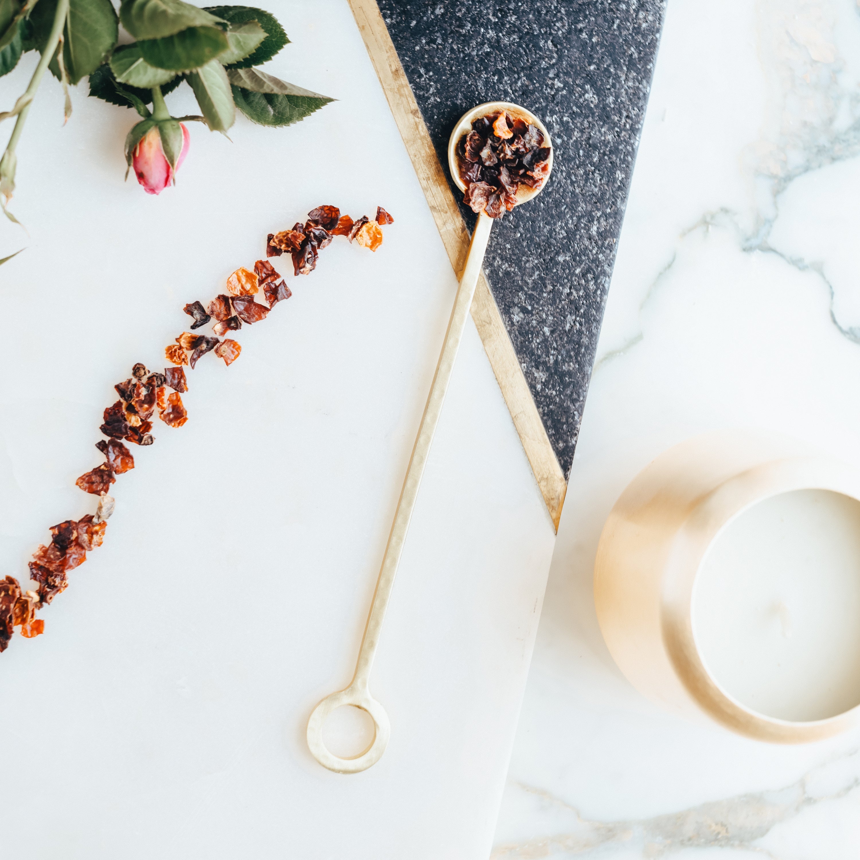Spoon with rosehips on a marble surface with flowers.