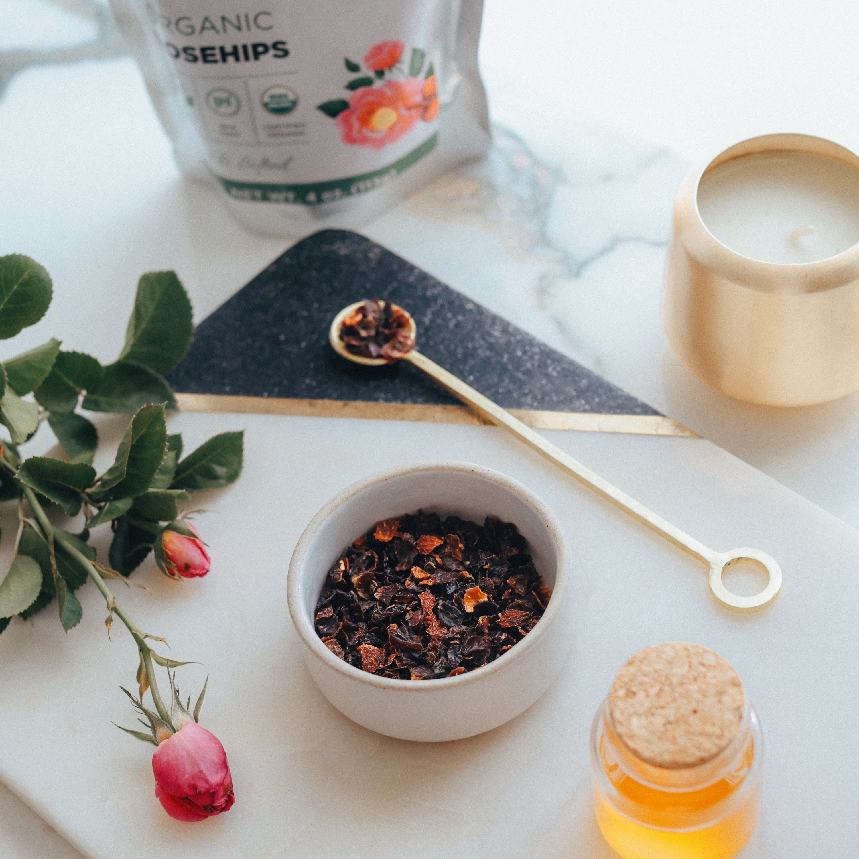 Rosehips in a bowl with a teacup, spoon, and candle on a table.