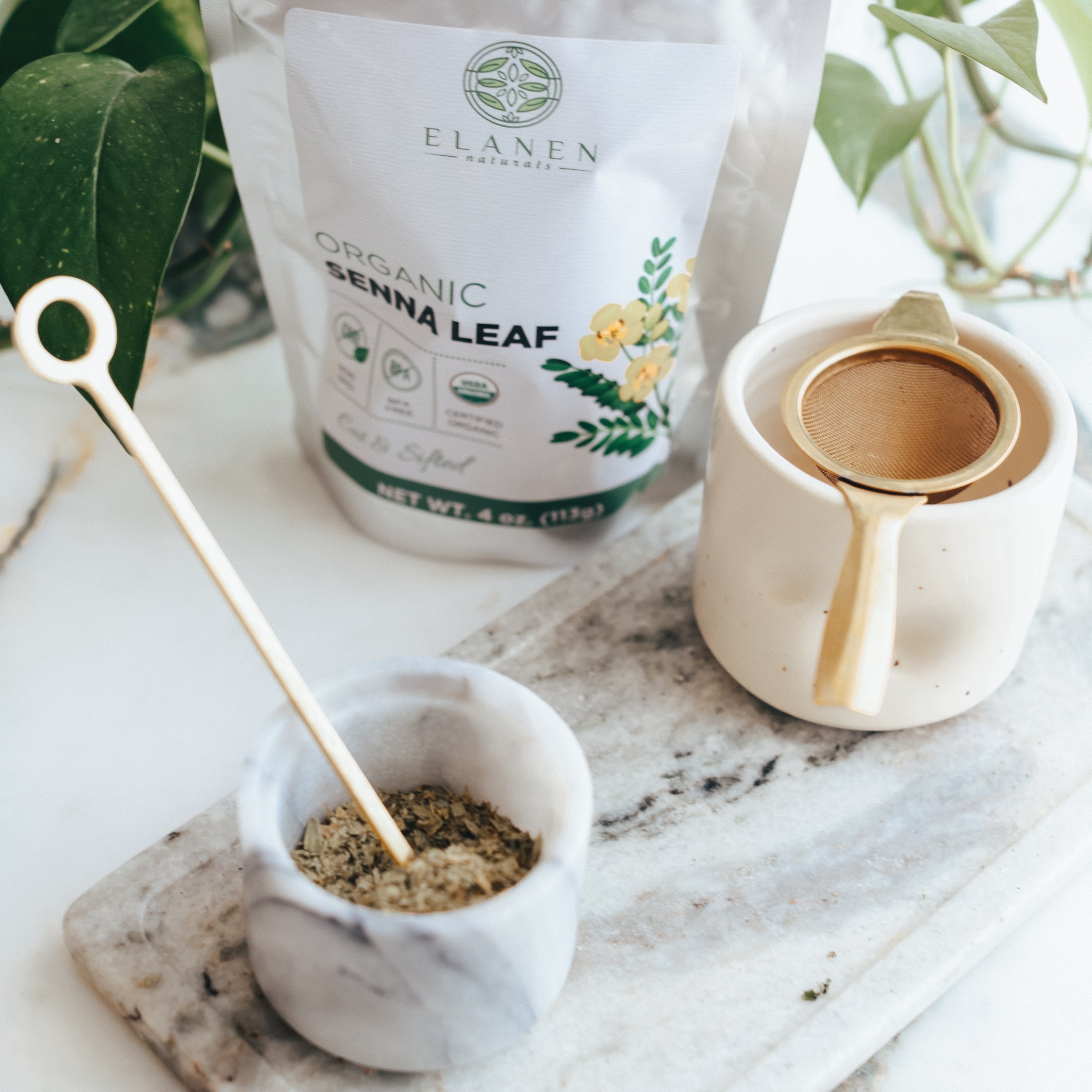 Senna leaf packaging with a small container of ground senna leaf on a marble surface.