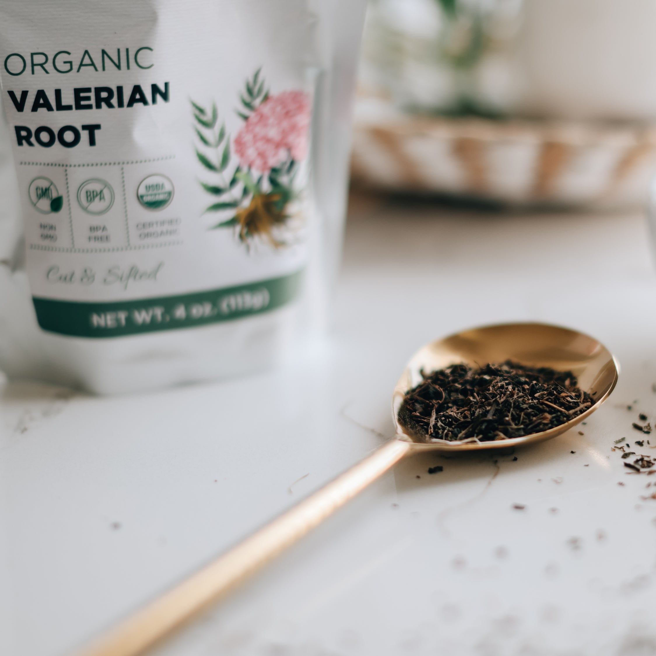 Bag of organic valerian root with a gold spoonful of dried valerian roots on a marble surface.