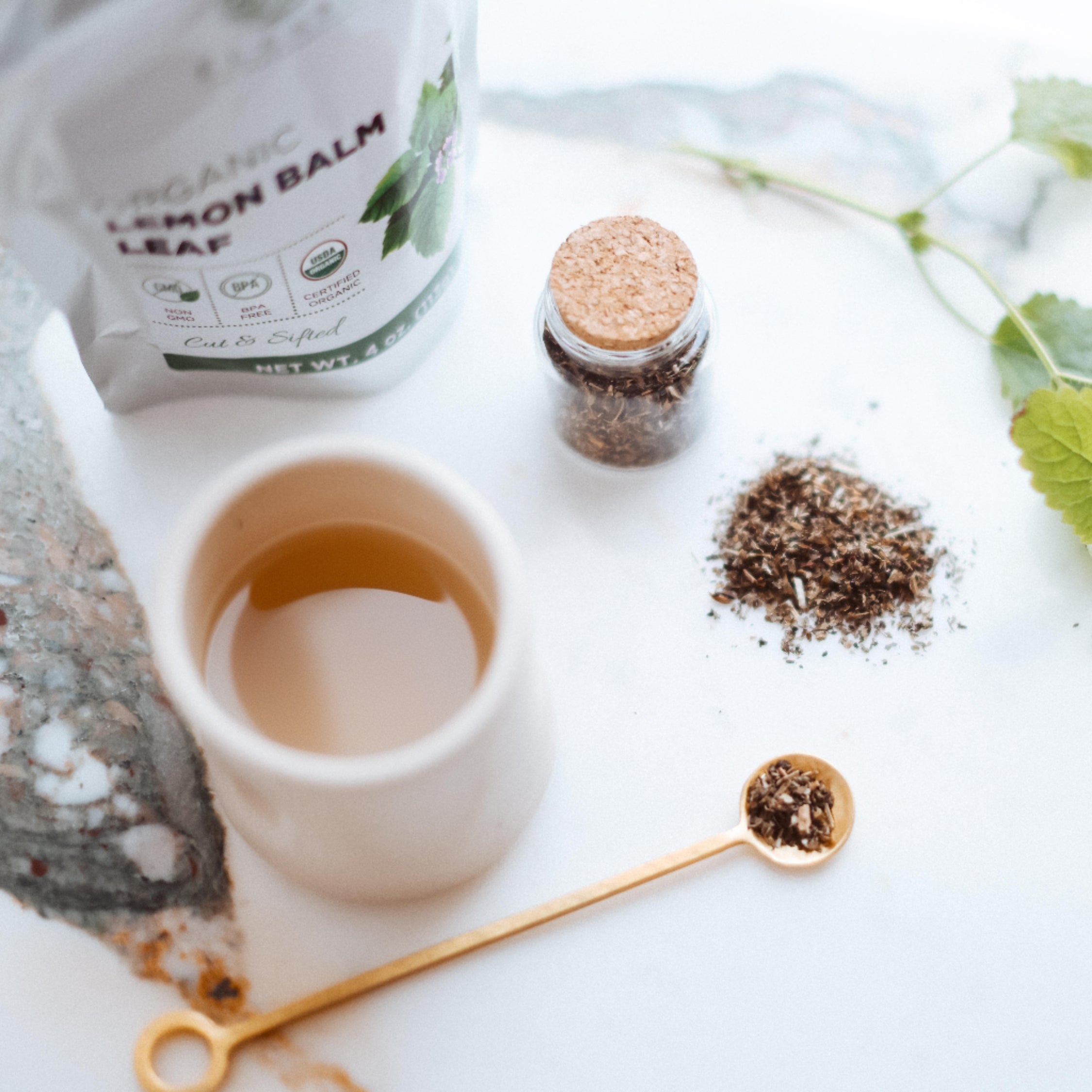 Tea-making setup with a tea bag, cup, and lemon balm leaf on a marble surface