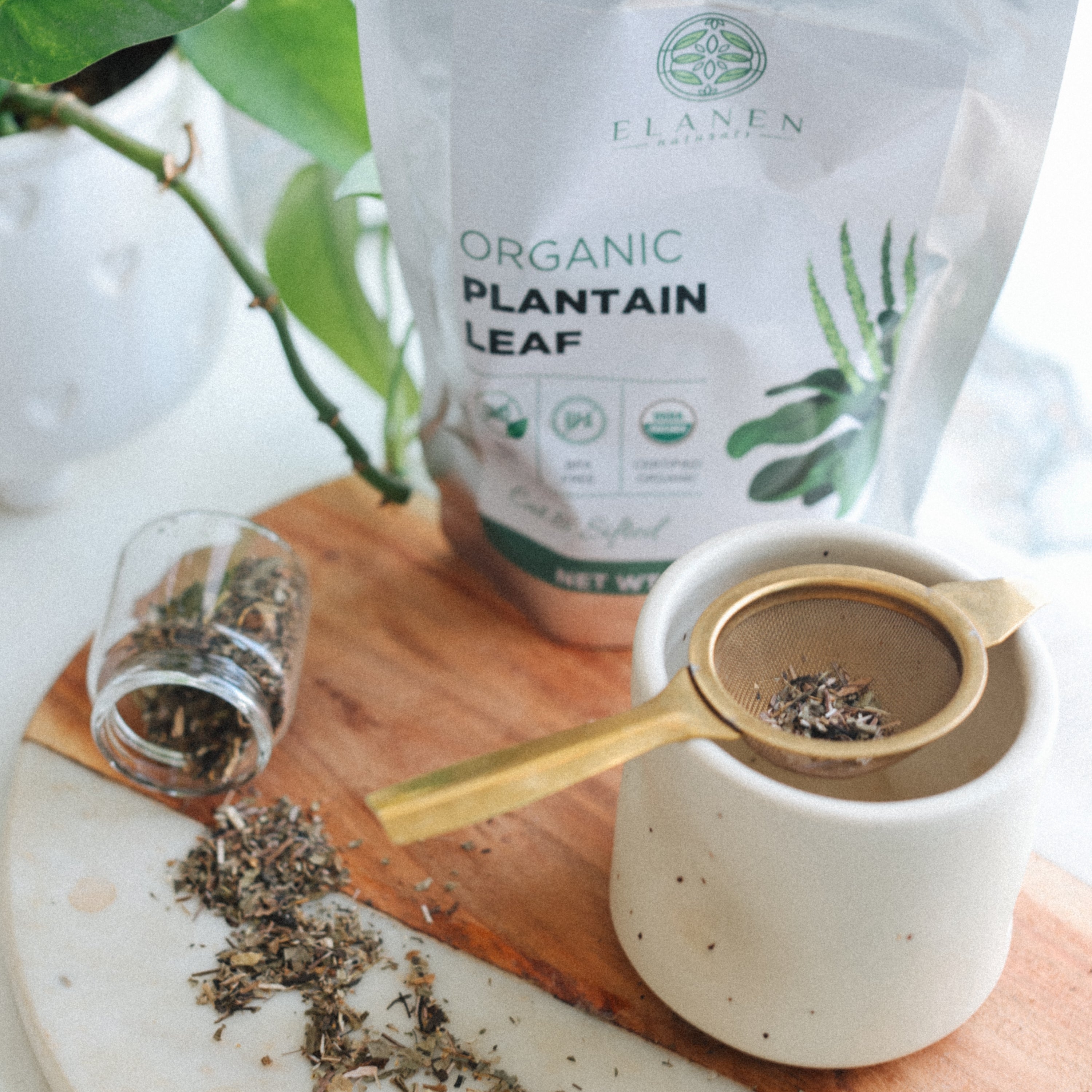 Elanen Organic Plantain Leaf packaging with a cup of tea and dried leaves on a wooden board.