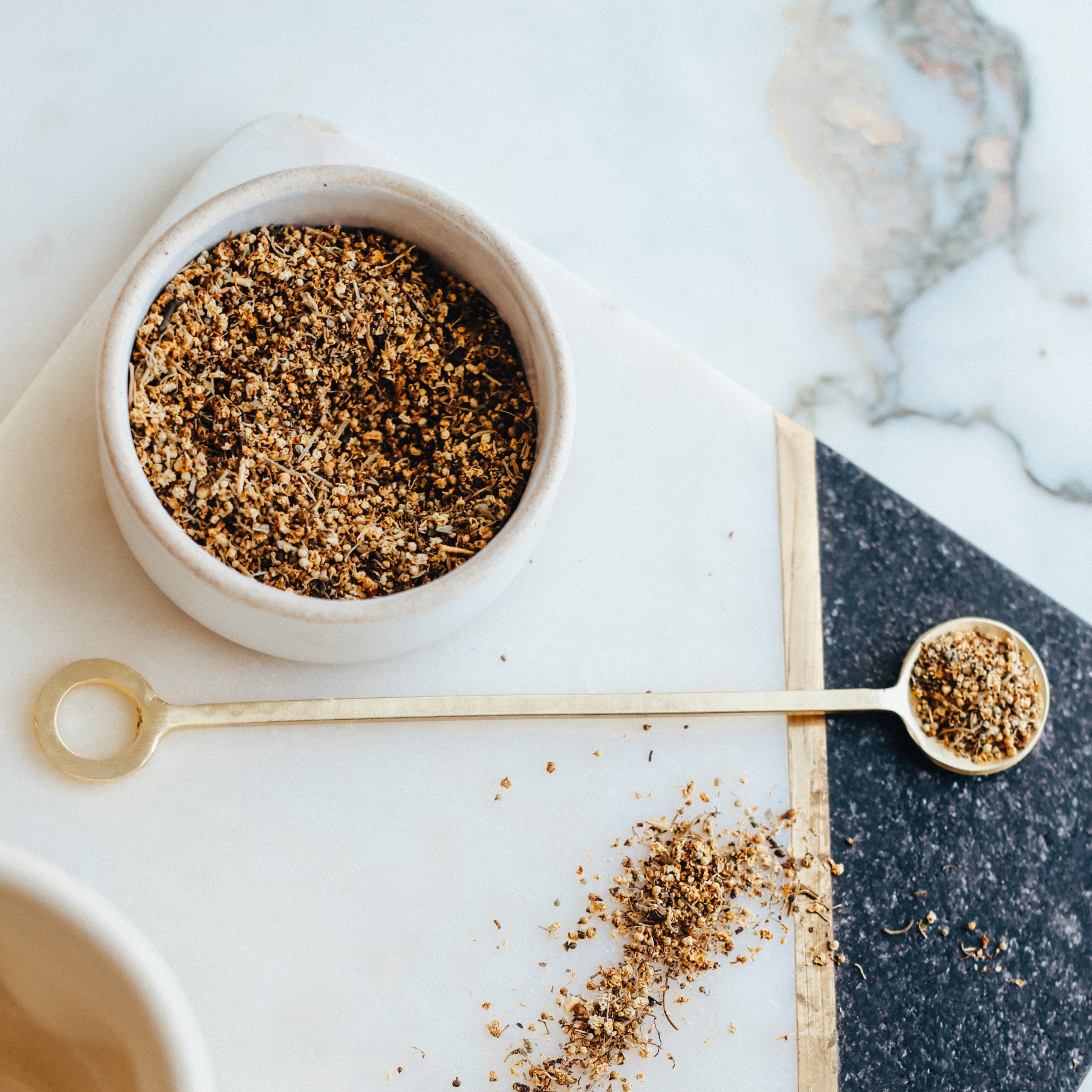 White bowl filled with elderflowers on a marble surface with a gold measuring spoon.