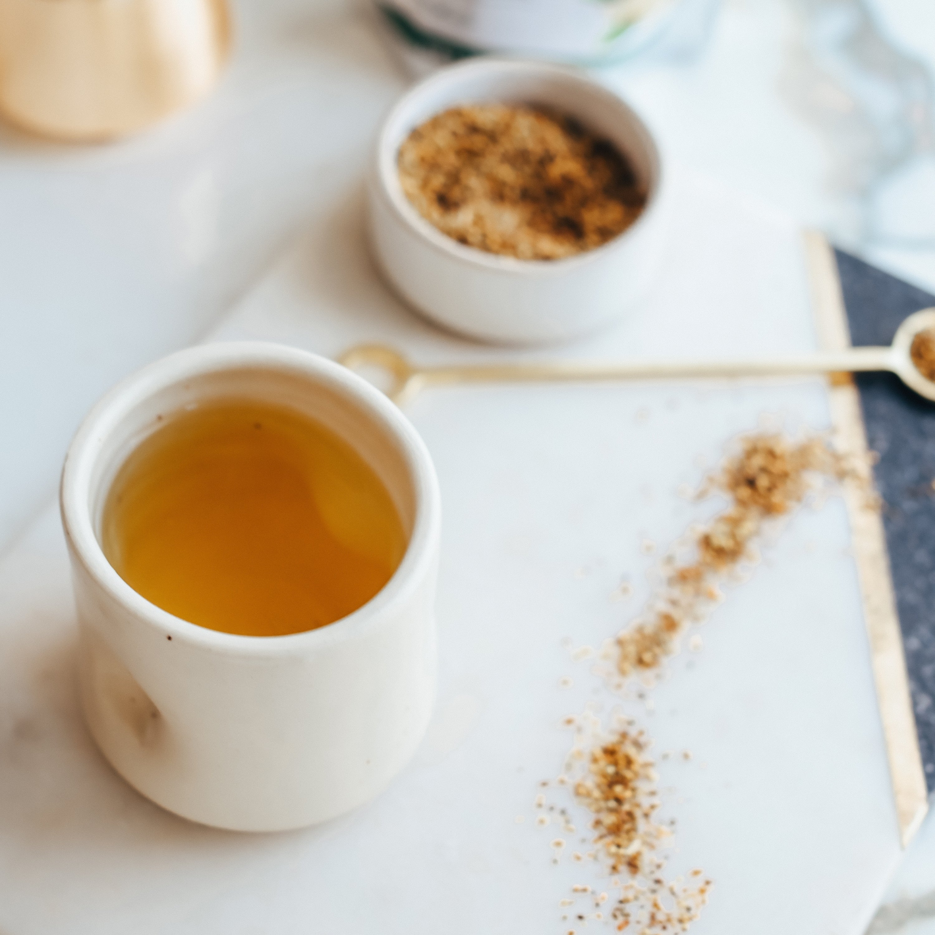White cup with yellow liquid on a marble surface with elderflowers.