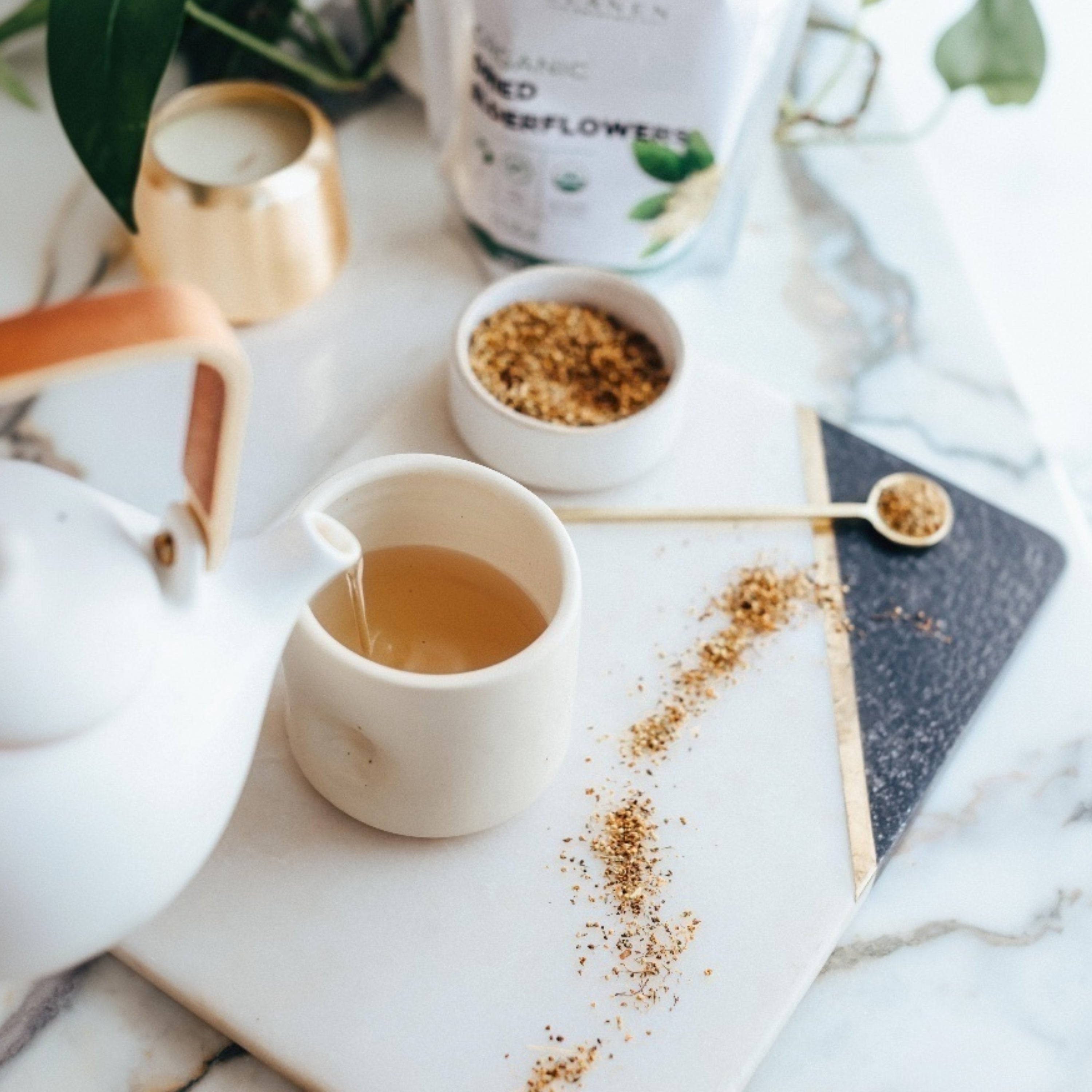 Tea cup with a spoon on a marble surface with a notebook and container in the background