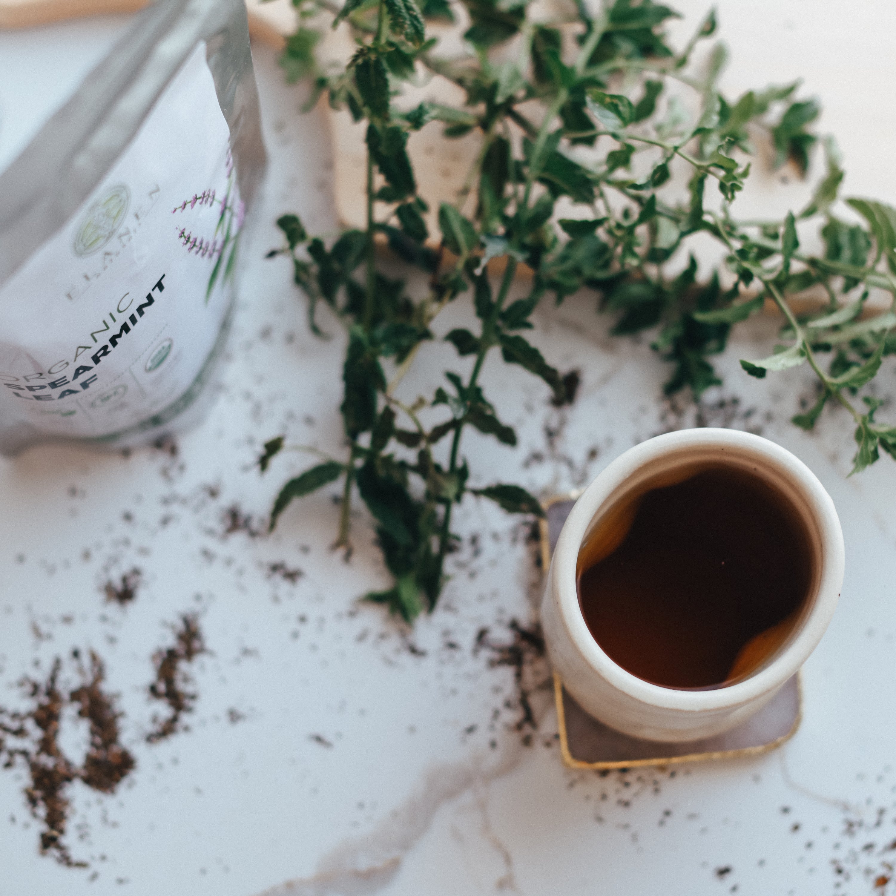 Cup of tea on a marble surface with a plant and a bottle in the background