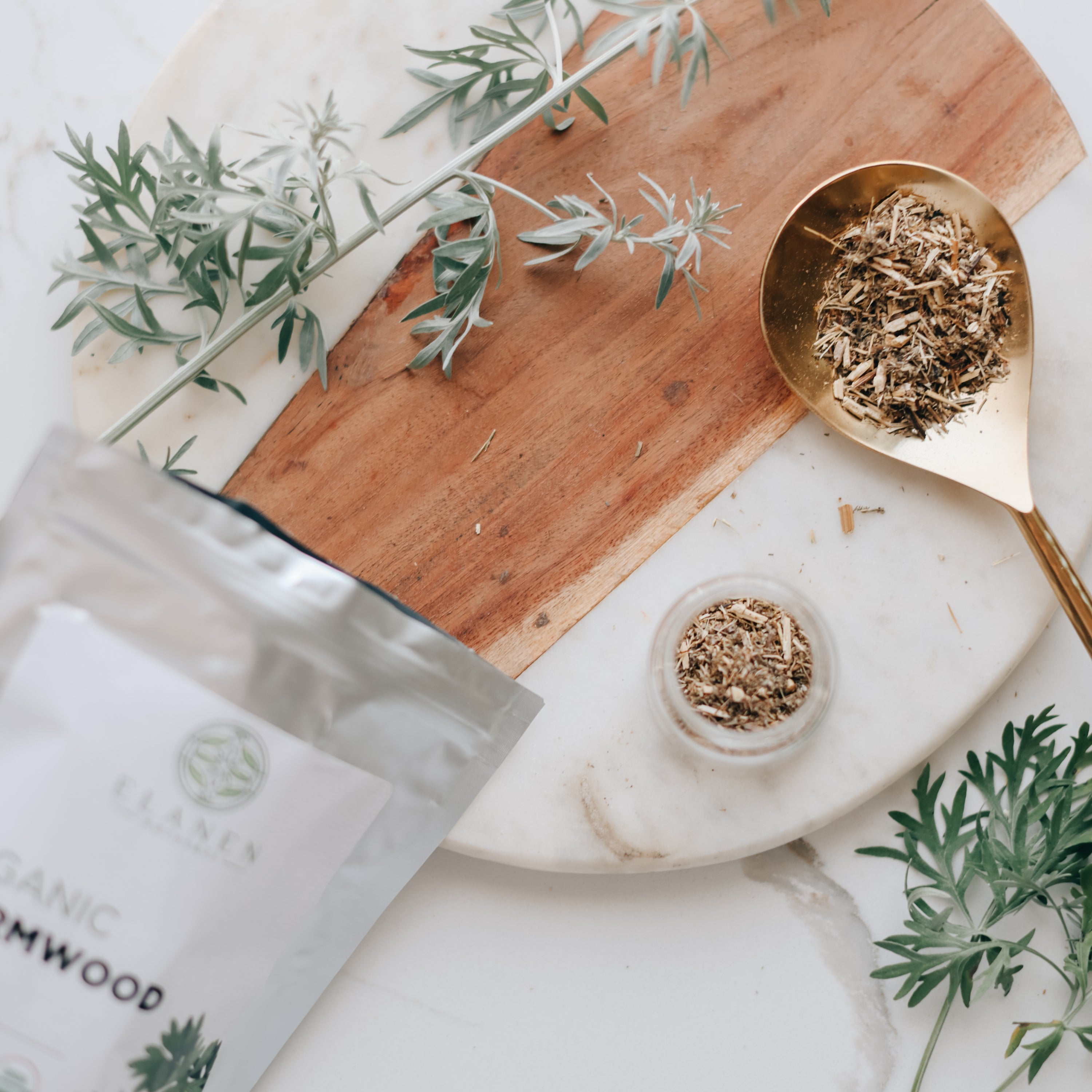 wormwood leaves on a wooden board with a marble surface, featuring a gold spoon and packaging.