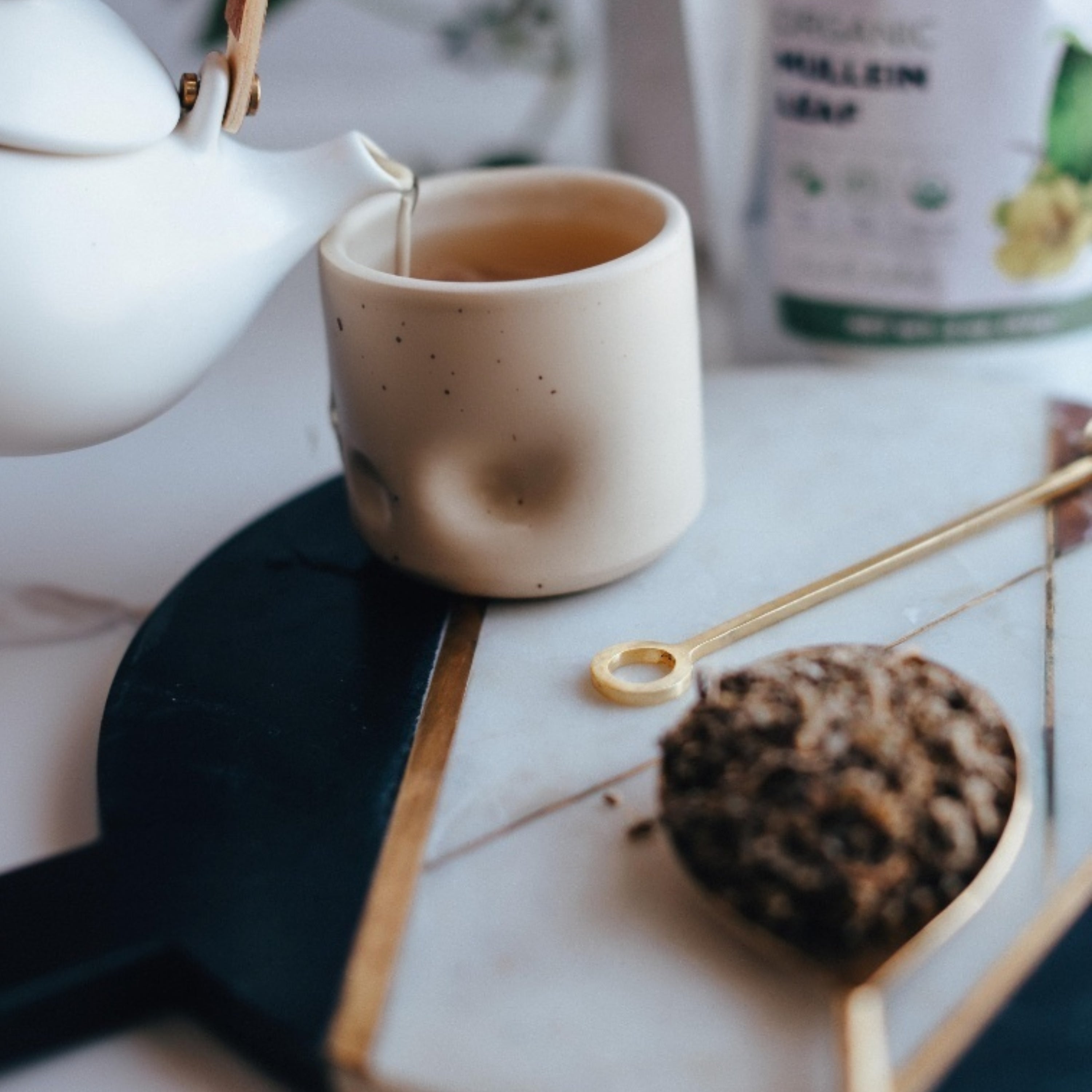 Tea being poured from a white teapot into a ceramic cup on a marble surface.