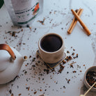Tea cup with loose tea leaves, cinnamon sticks, and a teapot on a marble surface.