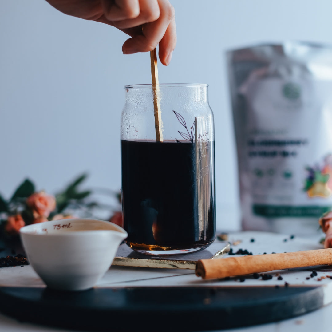 Hand stirring a glass of elderberry syrup with a stick on a table with a blurred background