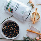 Tea packaging, bowl of elderberry syrup mix, and cinnamon sticks on a marble surface with flowers.