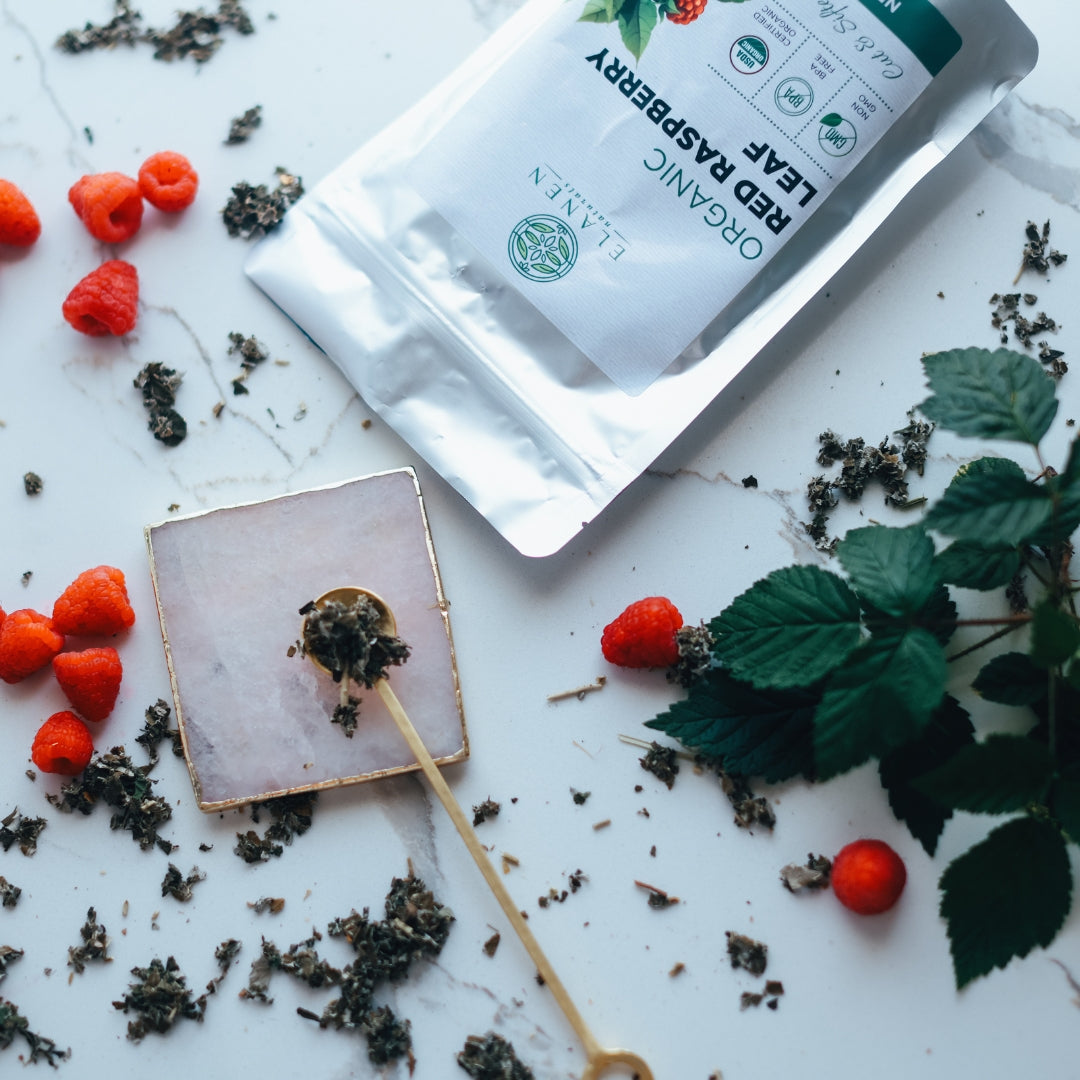 Tea packaging with red raspberries and tea leaves on a white surface