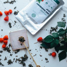Tea packaging with red raspberries and tea leaves on a white surface