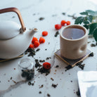 Tea set with a teapot, cup, and tea leaves on a light surface.