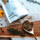 Tea packaging with a spoonful of tea leaves on a wooden board