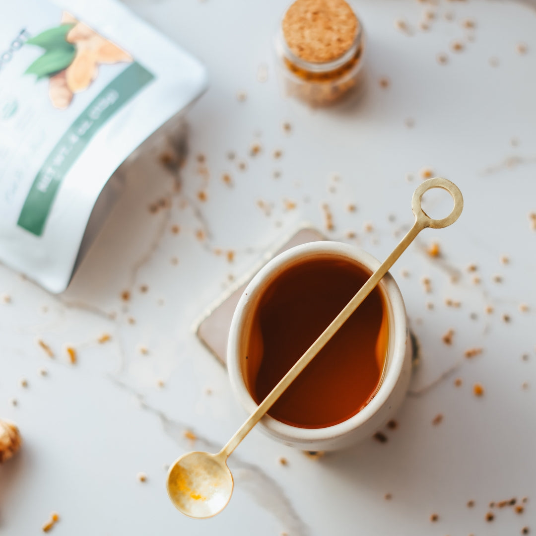 Cup of turmeric tea with a gold spoon on a light surface with scattered turmeric root 