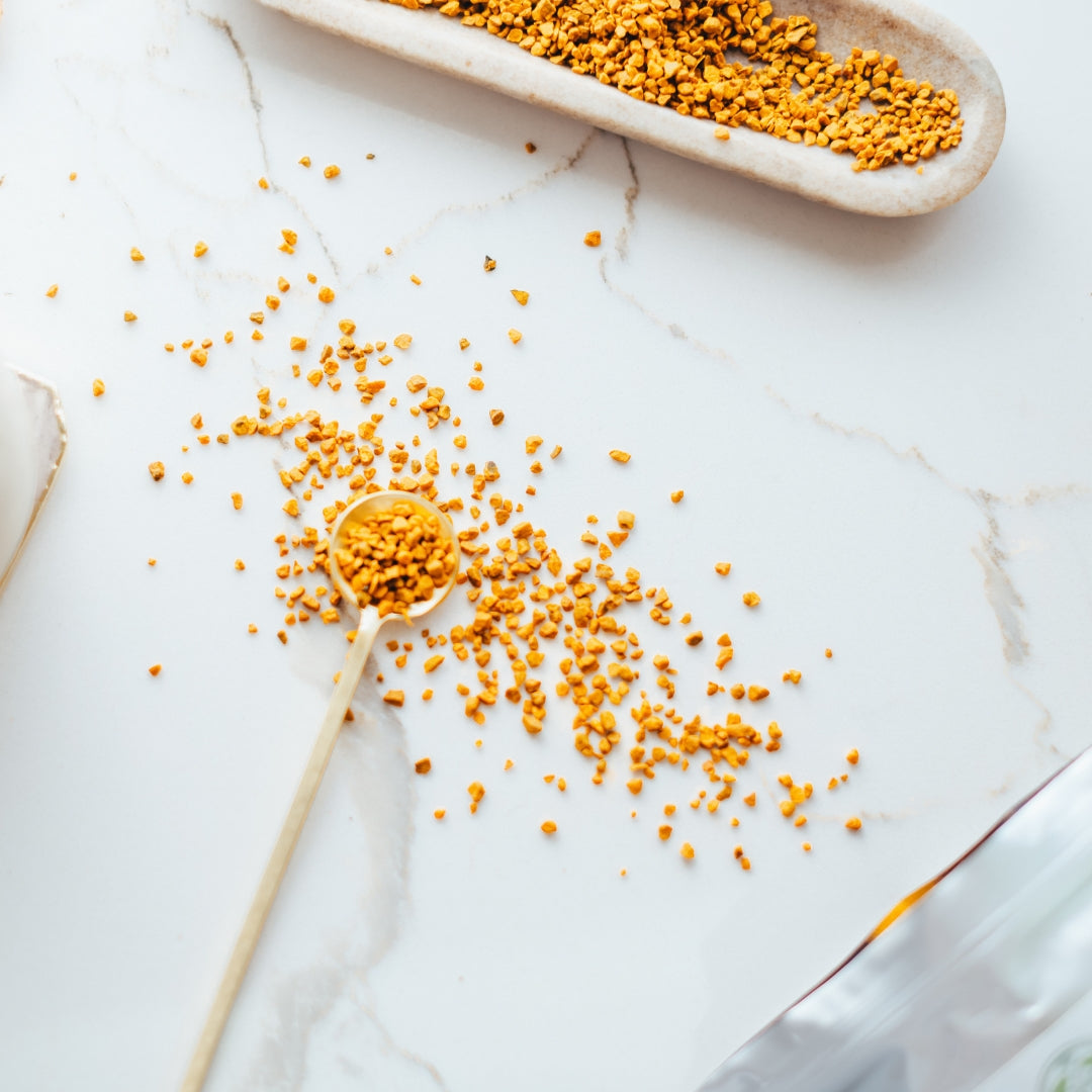 Yellow turmeric root on a white marble surface with a spoon and dish.