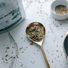 Gold spoon with dried herbs on a marble surface next to a bag of organic biloba leaf.
