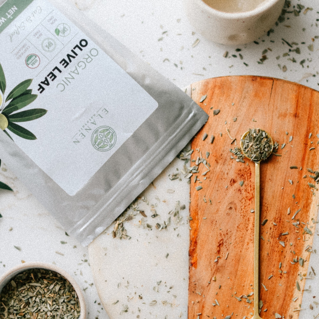 Olive leaf tea packaging with a wooden spoon and olive leaves on a light surface