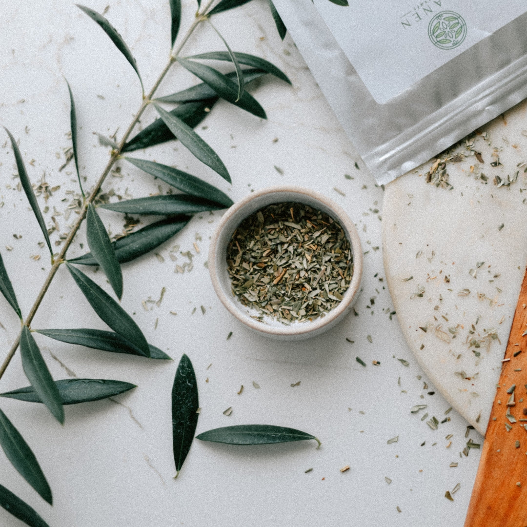 Herbal olive leaves in a small bowl with green leaves on a marble surface