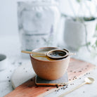 Brown ceramic cup with a small gold spoon on a white surface