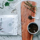Organic holy basil package on a marble surface with a wooden cutting board and herbs.