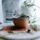 Ceramic cup on a marble surface with a plant and herbal packaging in the background