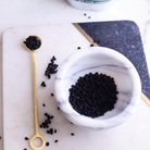 Black elderberries dried in a marble bowl with a gold spoon on a white surface