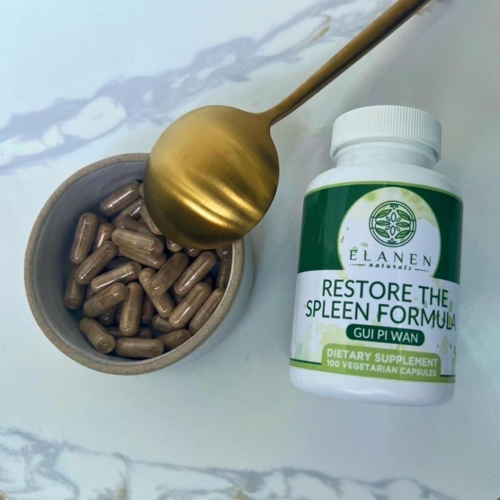 Supplement bottle labeled 'Restore the Spleen Formula' with capsules and a spoon on a marble surface.