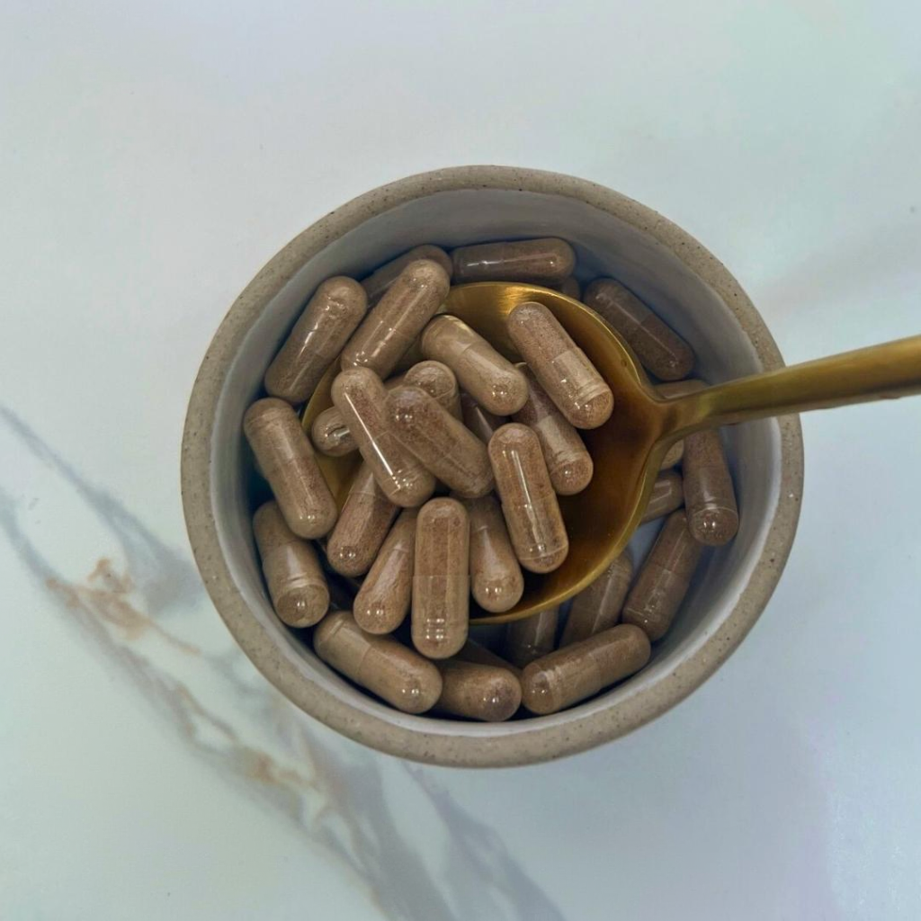 Brown capsules in a white bowl with a gold spoon on a light gray background