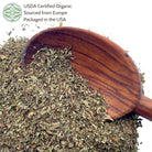 Wooden scoop filled with dried peppermint leaf on a white background.