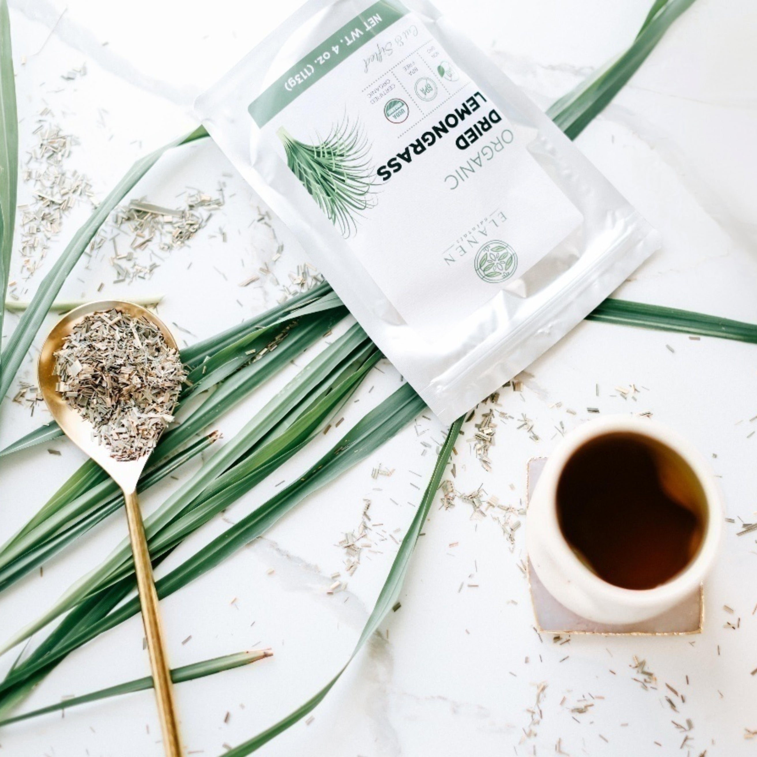 Herbal tea packaging with a spoonful of loose lemongrass and a cup on a white background