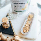 Organic ginger root with a jar of ground ginger and packaging on a marble surface.