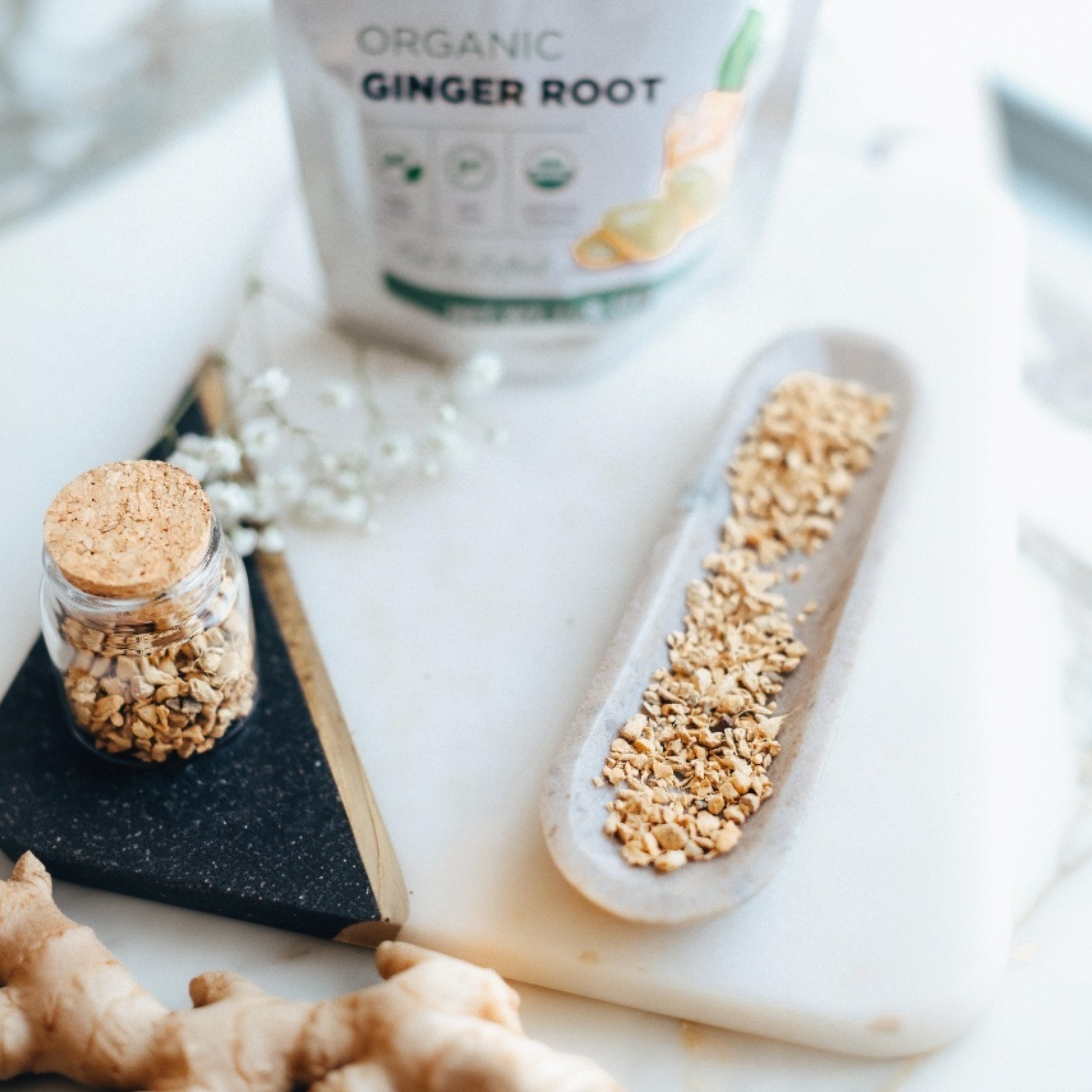 Organic ginger root with a jar of ground ginger and packaging on a marble surface.